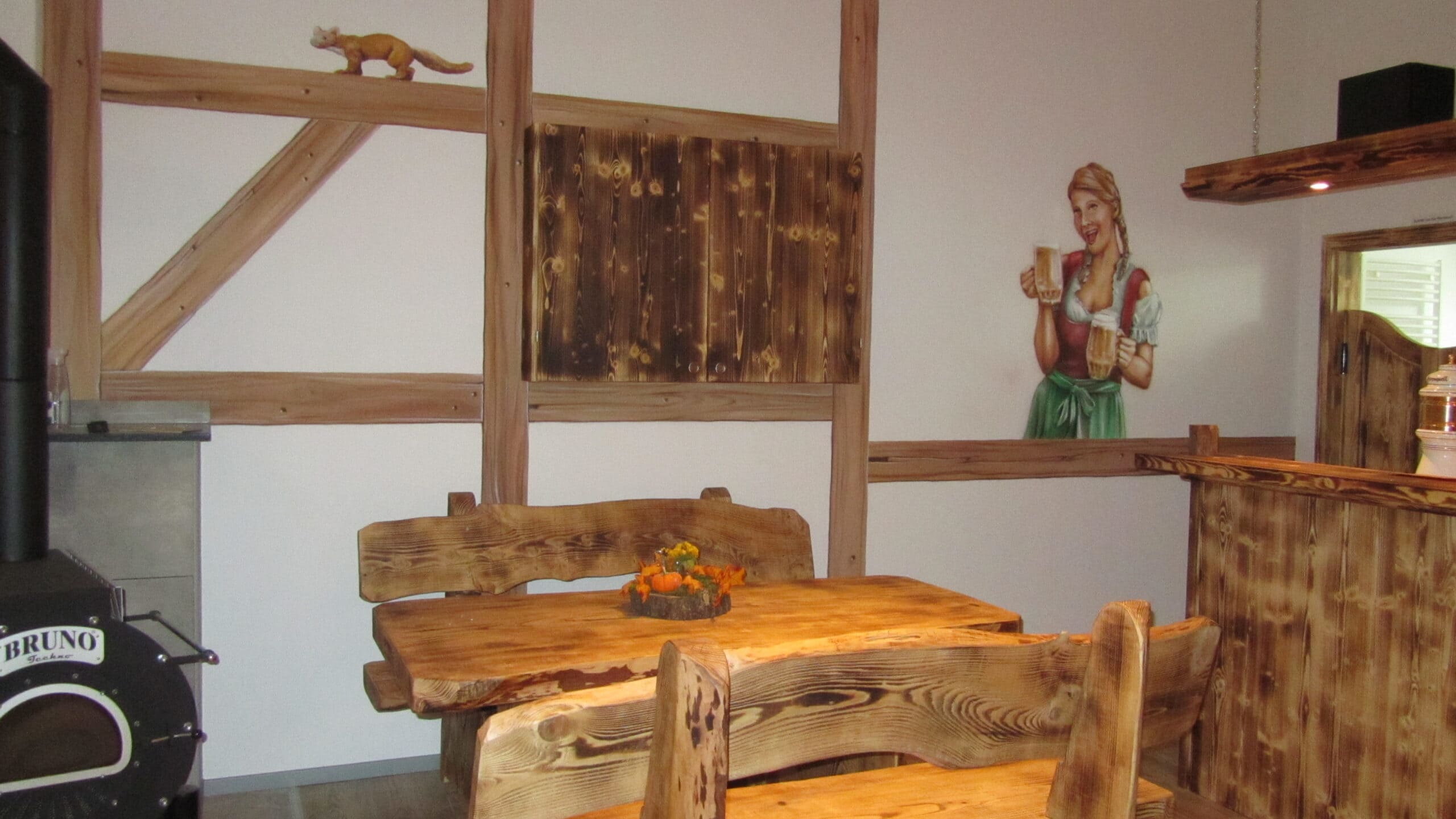 Bild eines Holztischs mit Holzbänken und Wandmalerei im Hintergrund